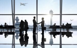 2 business people stood in an airport shaking hands, aeroplane in the background