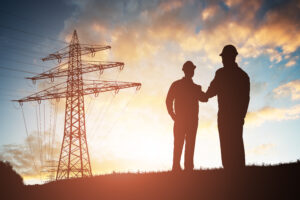 A silhouette of 2 engineers shaking hands, electricity pylons in the background