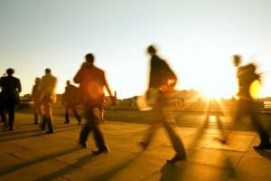 a blurred image of people walking down a street, a sunset in the background.