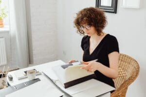 a young woman with glasses and curly hair is reading through a large file sat at a desk