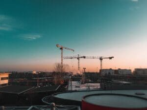 A picture of a construction site at dusk, 3 cranes in the background.