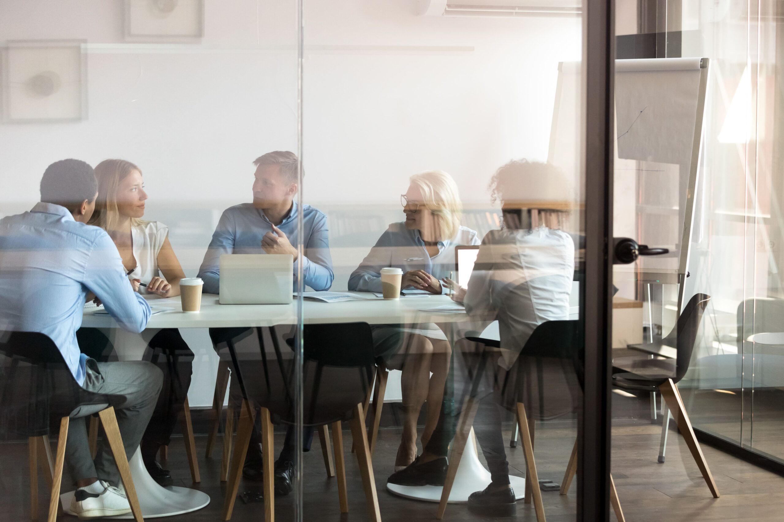 Group seated around a table discussing work in a glass-walled meeting room.