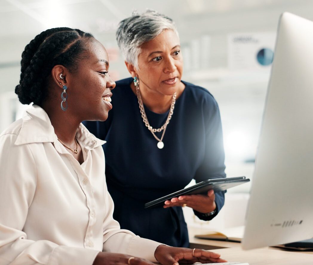 Two colleagues working together at a desk, reviewing information on a computer screen.