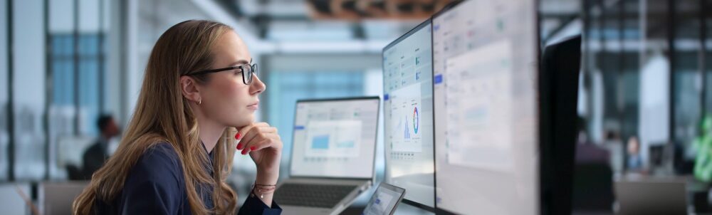 Person wearing glasses works at a desk using multiple computer screens and a laptop.